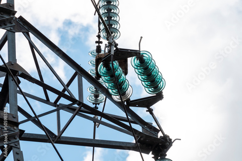 Close-up on a high voltage electric antenna, metal details and insulator chain, in a blue, cloudy sky