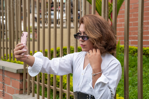 Wall Mural non-binary vain man taking selfie leaning on black gate in the street