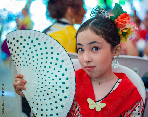 Beautiful asian little girl with traditional dress and hand fun in a stand at the Seville Fair in Spain photo