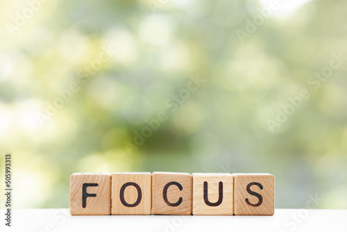Wooden cubes lie on a table on a green background. The cubes make up the word FOCUS.