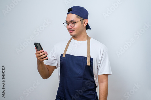 Portrait of cheerful handsome barista looking ahead and holding smartphone