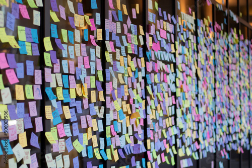 Colorful sticky notes with a variety of messages and emojis are seen on a storefront window at a university campus before graduation day.