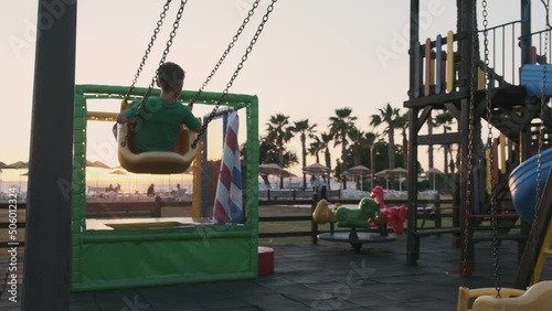 Boy rides on swings, in slowmotiom on a playgound on a tropical island at sunset photo