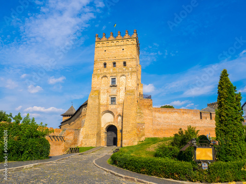 Lutsk High Castle, also known as Lubart's Castle. Ukraine. Brick Tower and Walls. A part of defence wall of Lutsk Castle. The Entrance tower against the blue sky and with greenery under a brick wall.