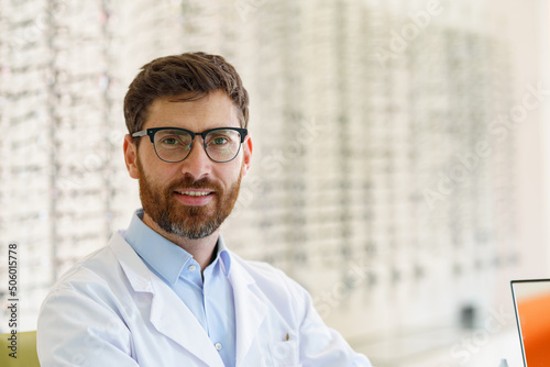 Canvastavla Handsome smiling ophthalmologist in front of the showcase with eyeglasses in the