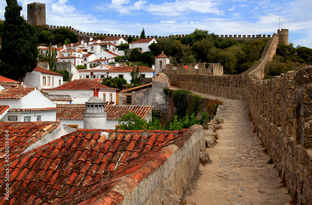White houses with red roofs and exotic trees surrounded by the walls of Castelo de Óbidos in Obidos, Portugal