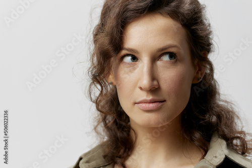 Closeup portrait of tricky pensive curly beautiful woman in casual khaki green shirt looks aside posing isolated on over white background. People Emotions Lifestyle concept. Copy space
