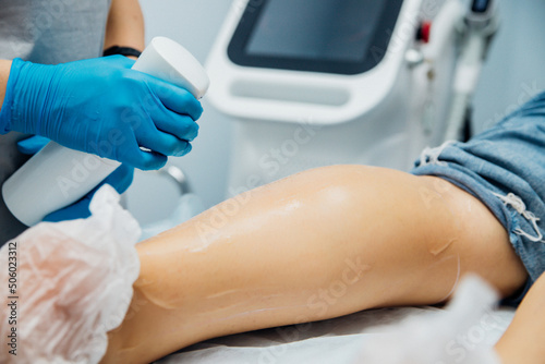 A master or cosmetologist in blue gloves prepares the client's skin, preparing for the epilation procedure. The concept of body care. Beauty salon. Moisturizing and nourishing the legs.