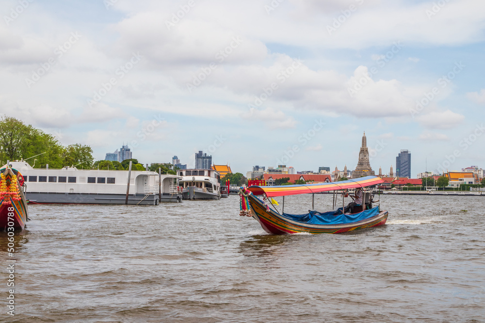 Fototapeta premium A longtail boat, the Chao Phraya River, the Thai royal first class Temple Wat Arun and the Cityscape of Bangkok Thailand Southeast Asia