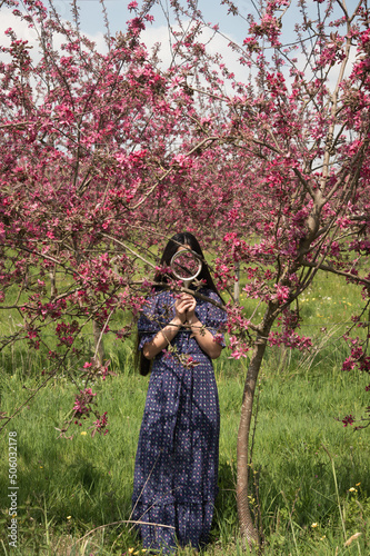 woman in classic blue dress standing in fruit orchard. with pink blossom hiding face iwith mirror photo