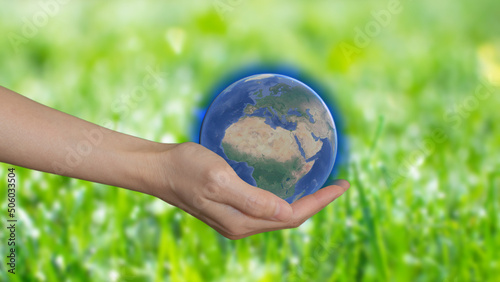 A woman's hand holding model of the planet on green background, earth day concept. Save the green world