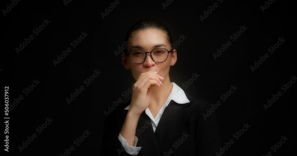 Positive business woman in glasses and office black and white clothes smokes an electronic cigarette during a break at work. Asian woman hovers on isolated black background and smiles at the camera Positive business woman in glasses and office black and white clothes smokes an electronic cigarette during a break at work. Asian woman hovers on isolated black background and smiles at the camera