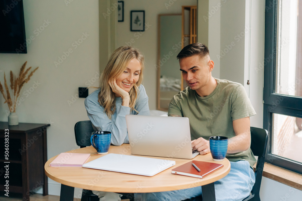 Young woman and man working on laptop while sitting at table at home. Young woman and man working on laptop while sitting at table at home.