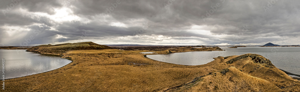 Panoramic, widescreen view of grassy hills and pseudocraters in around lake Myvatn in northern Iceland under a dramatic cloudy sky