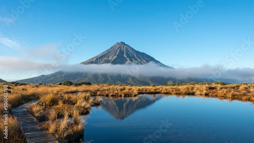 Mt Taranaki reflected in the clear water of Pouakai tarn, clouds drifting over the mountain, New Zealand.