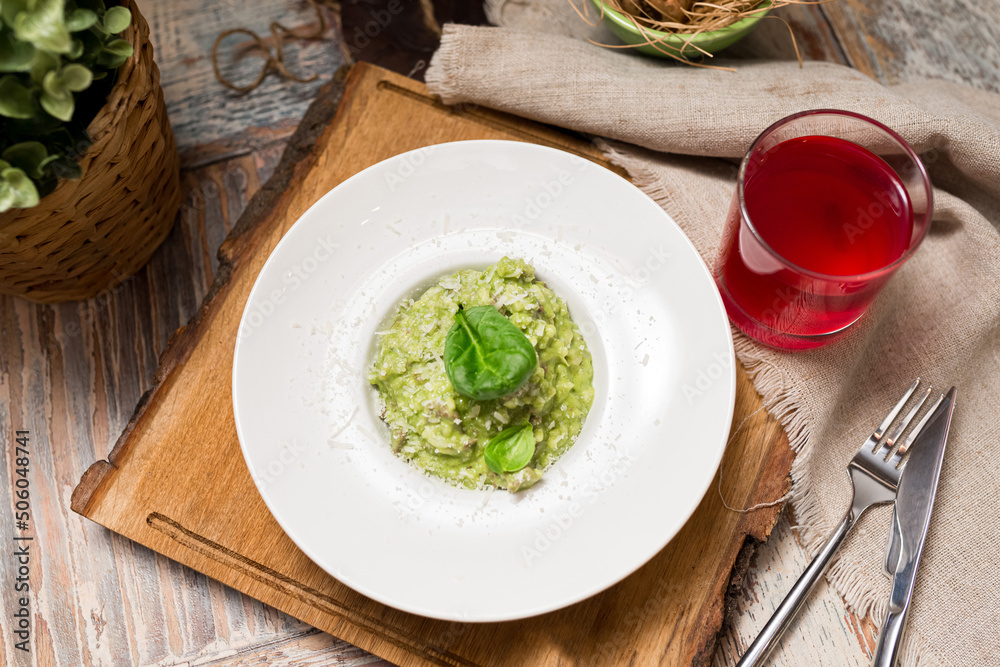 Plate serving of green risotto with basil leaves and cheese. Healthy food. Tender arborio flavored with spinach greens and infused with lamb meat broth Plate serving of green risotto with basil leaves and cheese. Healthy food. Tender arborio flavored with spinach greens and infused with lamb meat broth