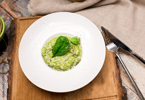 Plate serving of green risotto with basil leaves and cheese. Healthy food. Tender arborio flavored with spinach greens and infused with lamb meat broth photo