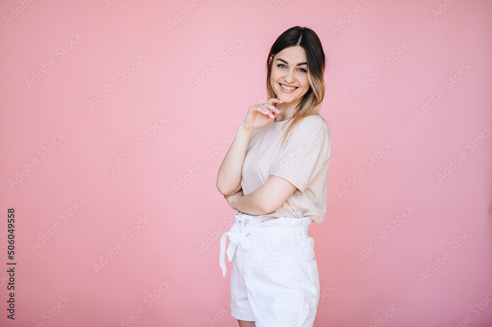Woman standing on a pink background in casual clothes and looking at the camera smiling broadly Woman standing on a pink background in casual clothes and looking at the camera smiling broadly