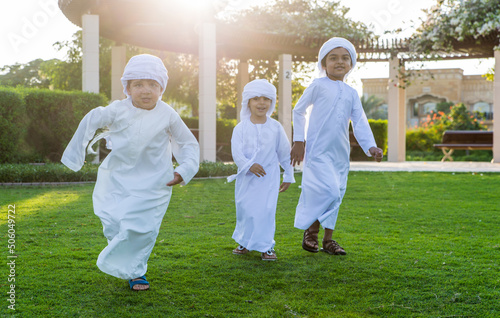 Children playing together in Dubai in the park. Group of kids wearing traditional kandura white dress from arab emirates photo