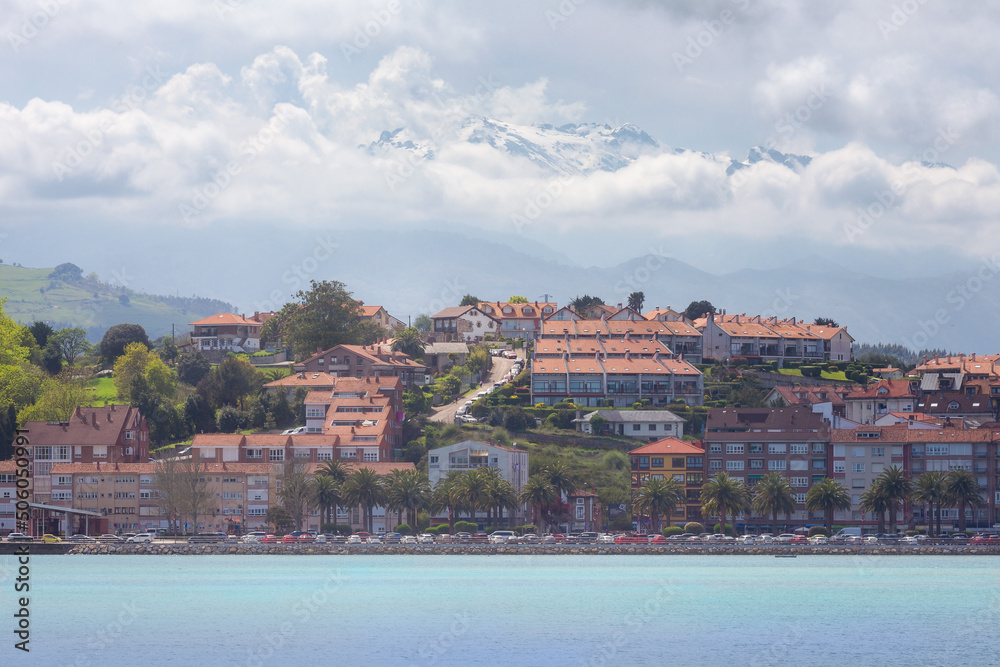 Vista de la localidad turística de San Vicente de la Barquera, Cantabria, España, con el mar azul al frente y los Picos de Europa tras las nubes, al fondo