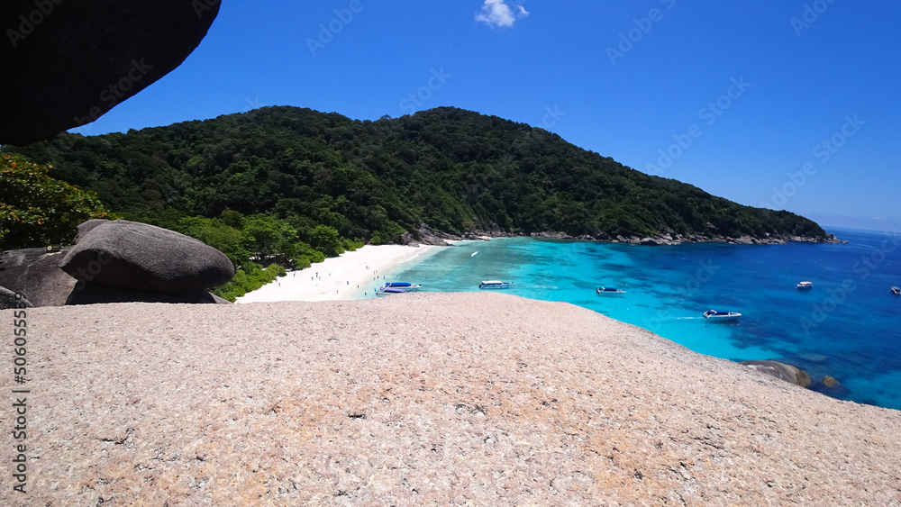 The guy is sitting on a rock and looking at the lagoon. A heavenly place on Earth - turquoise water, white sand, high rocks covered with trees. A place to relax. There are speedboats in the distance