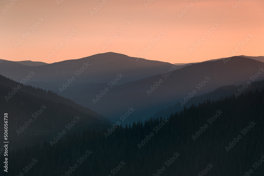 Amazing landscape of mountains at sunrise. View of orange sky and hills covered forest at mist.