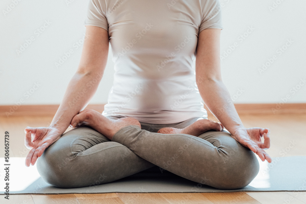 Cropped view of the senior woman in casual clothes meditating and sitting on lotus pose at home. Sport and recreation concept