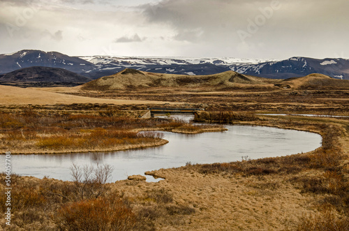 Landscape near lake Myvatn in Iceland, with hills, mountains, grass and shrubs and a road with a concrete bridge crossing a small river