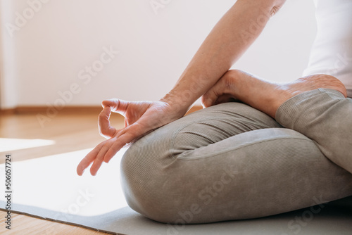 Cropped view of peaceful woman meditating in cozy room in lotus pose with mudra gesture. Calmness lifestyle concept