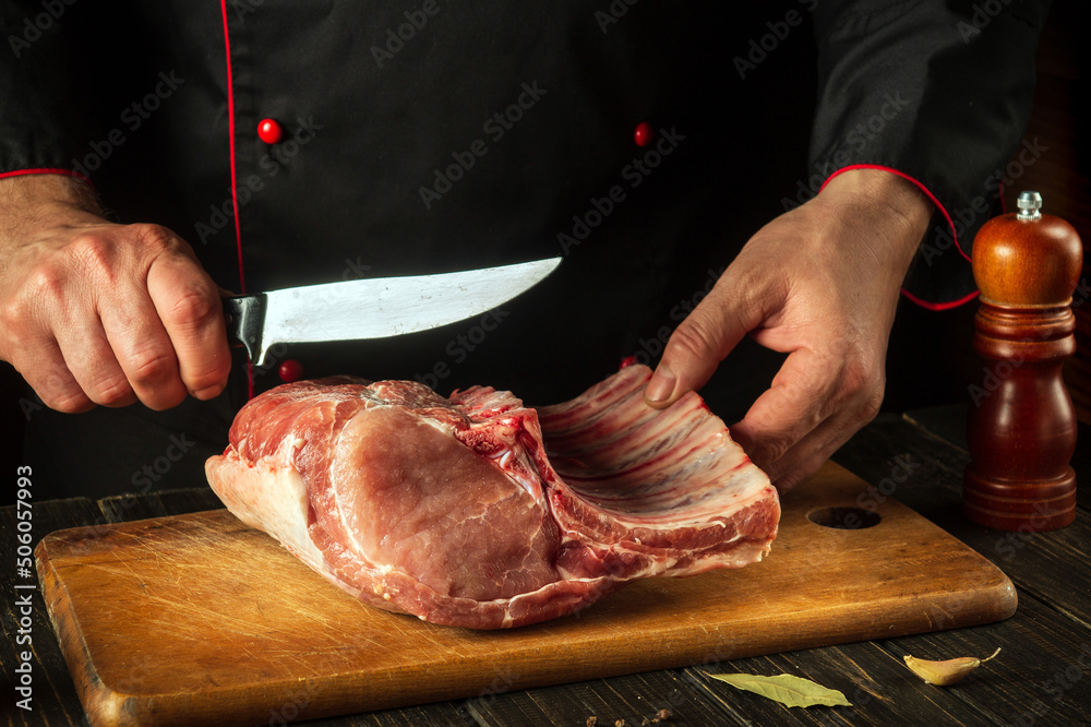 Butcher cuts raw ribs on a cutting board before grilling. European cuisine. Meat dish idea for a hotel