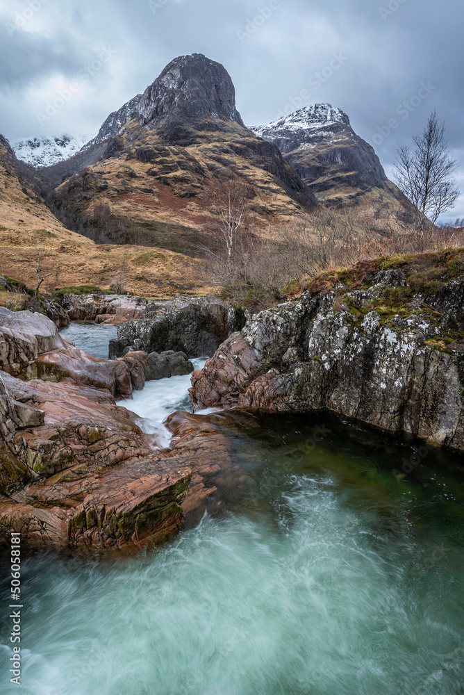 Gorgeous landscape image of vibrant River Coe flowing beneath snowcapped mountains in Scottish Highlands