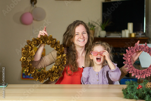 DIY Christmas wreath of cones. Woman and girl laughing happy together. concept of joyful parenthood little daughter. Natural materials for crafts. Babysitter plays with child cheerfully. sisters smile
