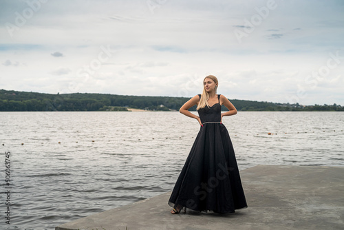 beautiful blonde girl in a black elegant fashionable dress stand near lake
