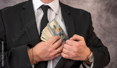 Businessman puts dollar banknote money in the pocket of his exquisite expensive suit.