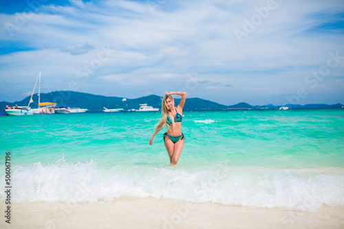 A young happy girl with a beautiful figure is standing in a bathing suit on the beach of an exotic island by the sea, a luxury resort, a concept of relaxation, vacation on a tropical beach in Thailand