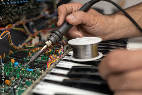 Hands of Latin American electronic technician repairing the circuit of a piano with soldering iron and tin in the service center. Concept repair, Music, electronic