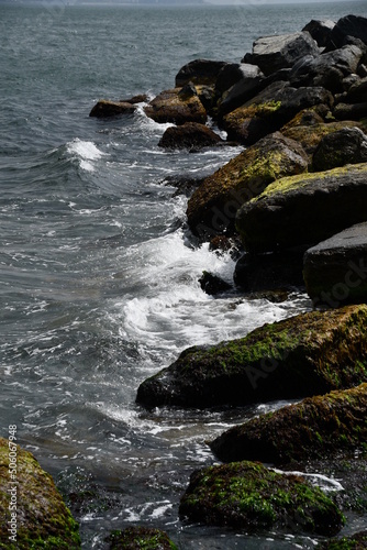 The coast of the sea bay with large stones. The waves crash on the rocks.