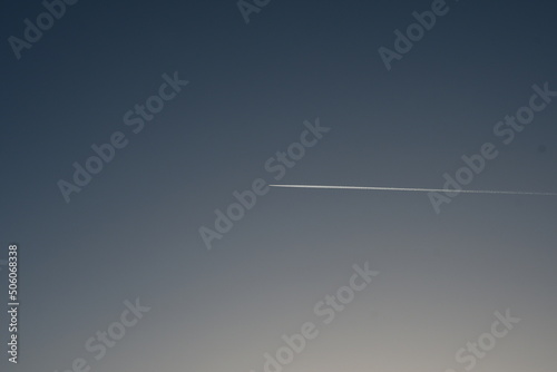 In the blue sky, a white trail from a flying plane. Blue sky background.