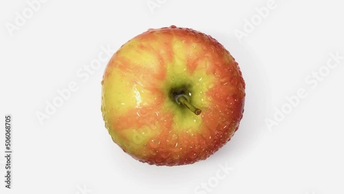 A red and yellow apple rotates on a white background in drops of water. Shooting is done from the top point. Fruit from the Fushi variety. photo