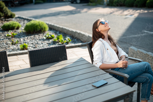 Relaxed woman with drink and mobile sitting on hotel terrace