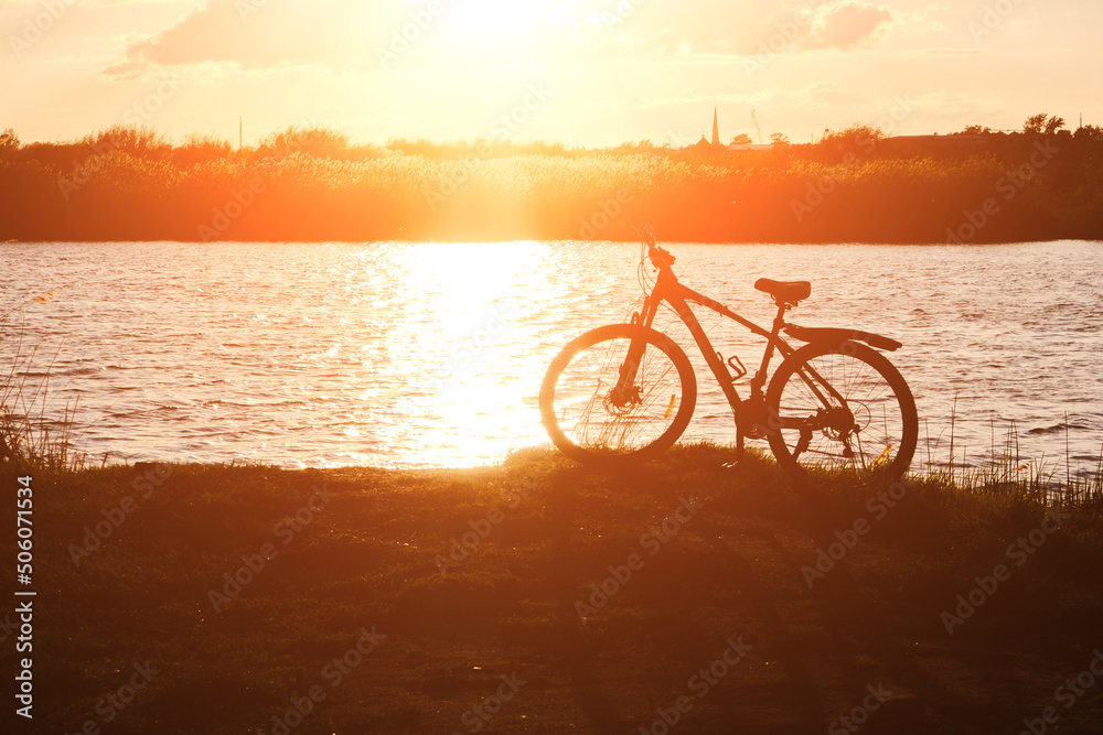 Fototapeta premium Silhouette bicycle against background river and bright red sunset.