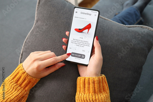 Closeup of woman doing online shopping on smartphone at home. Rear view of woman hand touching screen while selecting shoes on e commerce portal. Lady use e-commerce web shop to buy high heels. photo