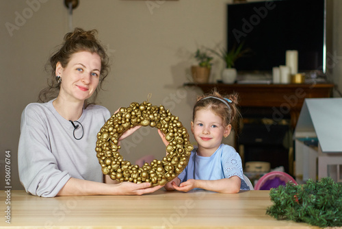 Christmas wreath of golden walnuts. woman and child smile close up. Make own golden nut for Cinderella. babysitter play with child. Mom and daughter together at home table. How to make wreath. DIY.