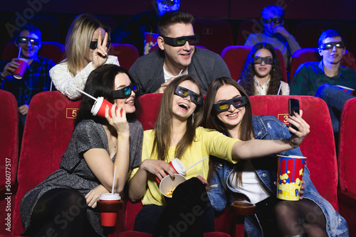 Three beautiful female friends laughing happily making a selfie together during a movie at the cinema