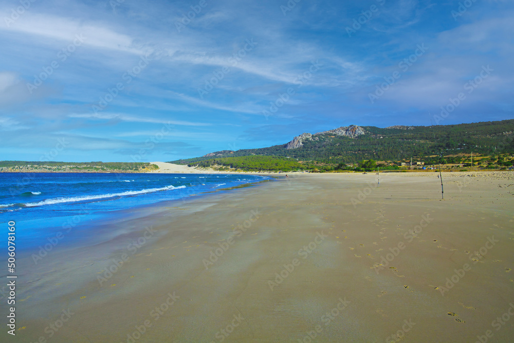 Tranquil morning empty sand beach scene, low tide, natural green hills, blue sky - Zahara de los Atunes, Costa de la luz, Spain