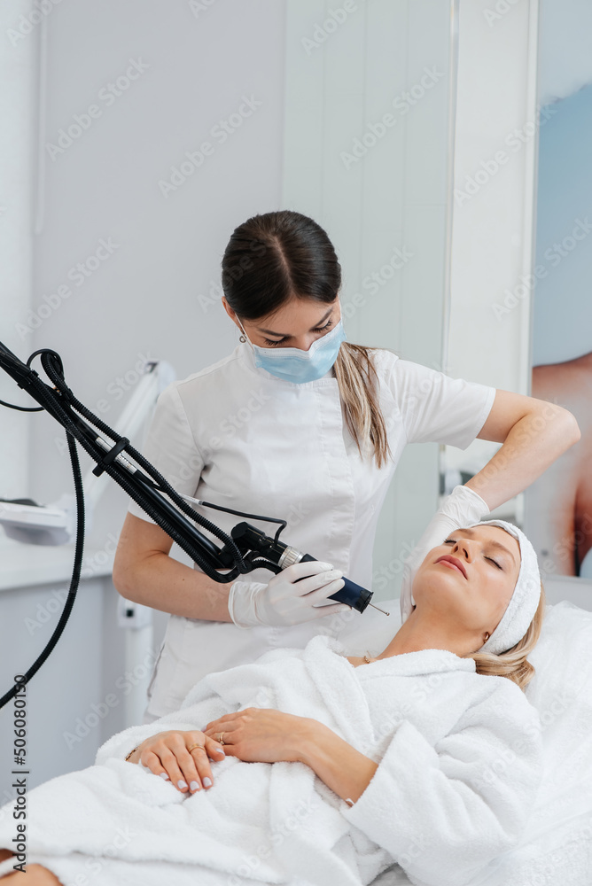 Obraz premium A young girl gets a carbon peeling for the skin of the neck in a beauty salon. Laser pulses cleanse the skin. Hardware cosmetology. The process of photothermolysis, warming the skin.