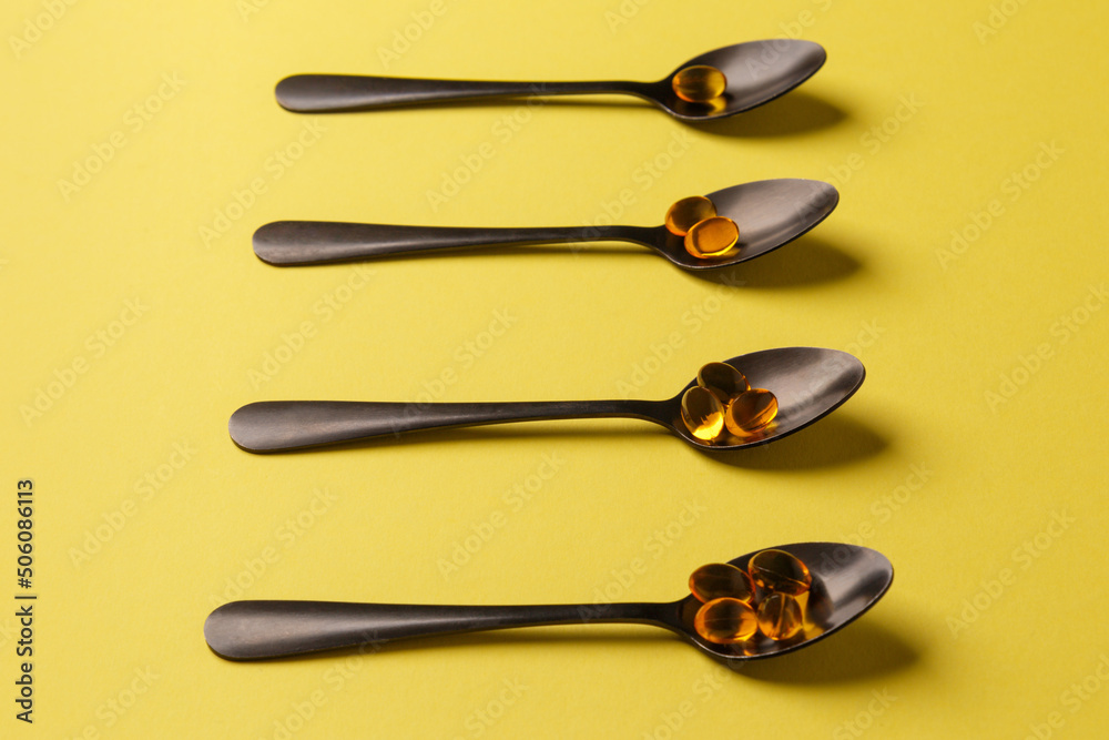 The concept of a healthy lifestyle. Fish oil - useful vitamin supplements on black metal spoons on a yellow background. Close-up, side view. Medical preparations. Natural additives. The concept of a healthy lifestyle. Fish oil - useful vitamin supplements on black metal spoons on a yellow background. Close-up, side view. Medical preparations. Natural additives.