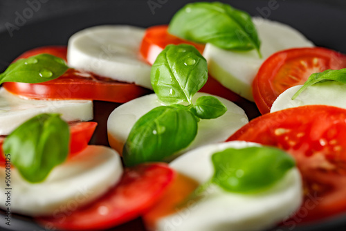 Caprese, Italian appetizer of mozzarella, basil and tomatoes, on gray plate, on dark background, selective focus.