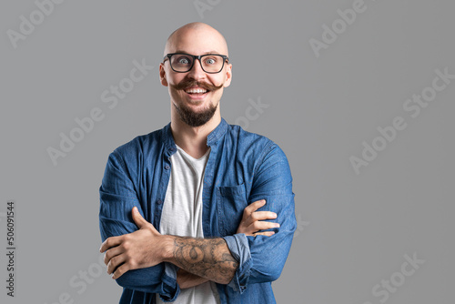 Studio shot of young happy man smiling with wide open eyes while wearing eyeglasses with arms crossed