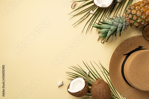 Summer holidays concept. Top view photo of hat fresh tropical fruits cracked coconuts pineapple and green palm leaves on isolated beige background photo